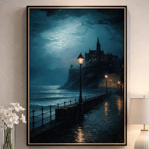 May include: A framed art print depicts a coastal scene at night. A stone pier with lampposts leads to a distant castle on a cliff. The artwork is in shades of blue and gray, with the moon illuminating the water and sky.