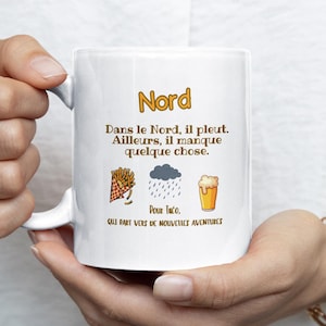 Peut inclure: Mug en céramique blanche avec le mot "Nord" et du texte en français. Le mug présente des illustrations de frites, de pluie et de bière. Le mug est tenu par une personne portant une bague et un bracelet dorés.