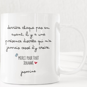 Pode incluir: Caneca de cerâmica branca com uma alça curva. A caneca apresenta texto manuscrito preto em francês, incluindo "Merci pour tout Johanne" e o nome "jasmine". Um pequeno coração vermelho também é visível.