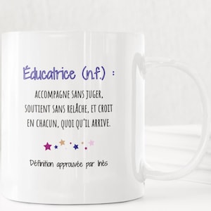 Pode incluir: Caneca de cerâmica branca com uma alça grande. A caneca apresenta texto em roxo e preto, incluindo "Educatrice (n.f.):" e uma definição. O design inclui estrelas e as palavras "Définition approuvée par Inès".