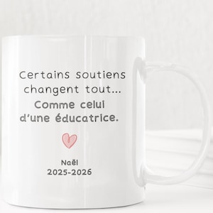 Pode incluir: Caneca de cerâmica branca com uma alça curva. A caneca apresenta o texto "Certains soutiens changent tout... Comme celui d'une éducatrice." e um coração rosa. Abaixo do coração está o texto "Noël 2025-2026."