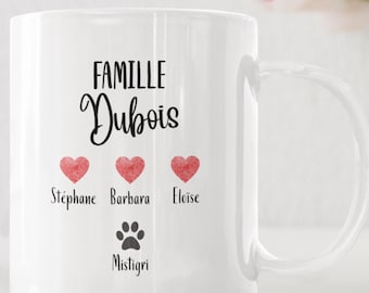 May include: White ceramic mug with the text "FAMILLE Dubois" in black script. Below are three red watercolor hearts with names Stéphane, Barbara, and Eloïse. A paw print and the name Mistigri are below the hearts. A gift box logo is in the top left corner.