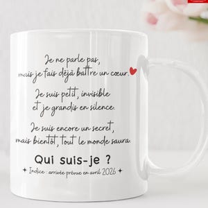 May include: White ceramic mug with black text in French, including the phrases "Je ne parle pas" and "Qui suis-je ?" A red heart is next to the first line. The mug has a curved handle and is on a white surface.