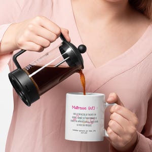 Pode incluir: Uma prensa francesa despeja caf&eacute; em uma caneca branca. A caneca tem texto em franc&ecirc;s que diz "Ma&icirc;tresse (nf.)" e uma defini&ccedil;&atilde;o. A prensa francesa &eacute; preta e de vidro. O caf&eacute; &eacute; marrom escuro.