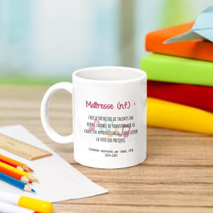 Pode incluir: Caneca de cer&acirc;mica branca com o texto "Ma&icirc;tresse (n.f.): CHEF D'ORCHESTRE DE TALENTS EN HERBE, CAPABLE DE TRANSFORMER LE CHAOS EN APPRENTISSAGES SANS LEVER LA VOIX (OU PRESQUE)." Rodeada por l&aacute;pis de cor, uma r&eacute;gua e livros.