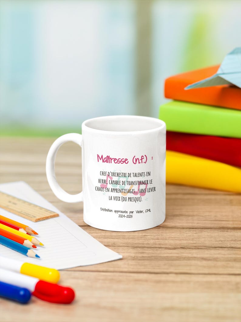 Pode incluir: Caneca de cer&acirc;mica branca com o texto "Ma&icirc;tresse (n.f.): CHEF D'ORCHESTRE DE TALENTS EN HERBE, CAPABLE DE TRANSFORMER LE CHAOS EN APPRENTISSAGES SANS LEVER LA VOIX (OU PRESQUE)." Rodeada por l&aacute;pis de cor, uma r&eacute;gua e livros.