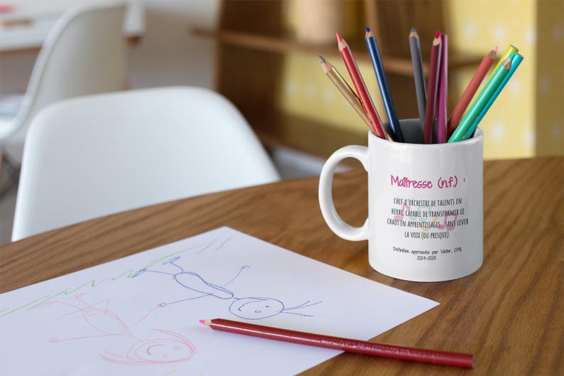 Pode incluir: Uma caneca de cer&acirc;mica branca com l&aacute;pis coloridos, com o texto "Ma&icirc;tresse (nf)" e outro texto em franc&ecirc;s. Um desenho e um l&aacute;pis vermelho est&atilde;o sobre a mesa de madeira. Um item tem&aacute;tico para professores.