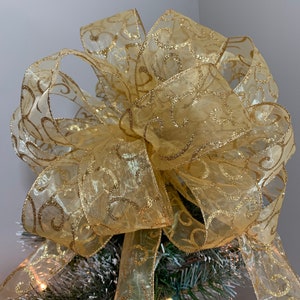 May include: A gold glitter Christmas tree topper bow made of sheer ribbon with a swirl pattern.