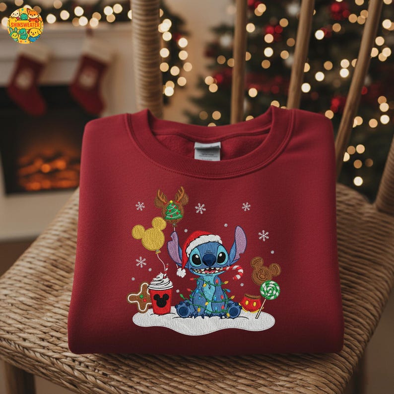 K&ouml;nnte beinhalten: Ein weinrotes Sweatshirt mit einem gestickten Design der Figur Stitch aus Lilo & Stitch, gekleidet mit einem Weihnachtsmannhut und umgeben von weihnachtlichen Elementen. Das Design umfasst einen Mickey Mouse-Ballon, Lebkuchen und eine Zuckerstange.