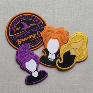 Może przedstawiać: Okrągła haftowana naszywka z napisem Premium Witches Brew Est. 1693 Sanderson Sisters Brewing Co. Salem, MA oraz fioletowym kapeluszem czarownicy, obok trzech haftowanych naszywek przedstawiających stylizowane postacie z pomarańczowymi, fioletowymi i żółtymi włosami.