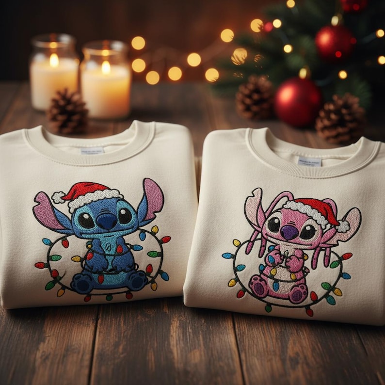Pu&ograve; includere: Due felpe color crema con personaggi di cartoni animati ricamati che indossano cappelli di Babbo Natale e luci natalizie. Un personaggio &egrave; blu, l'altro rosa. Le felpe sono su una superficie di legno, con candele e decorazioni natalizie sullo sfondo.