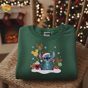 K&ouml;nnte beinhalten: Dunkelgr&uuml;nes Sweatshirt mit einem gestickten Bild von Stitch aus Lilo & Stitch, der einen Weihnachtsmannhut tr&auml;gt und von Weihnachtsdekorationen umgeben ist. Das Design umfasst Schneeflocken, Luftballons und Zuckerstangen.