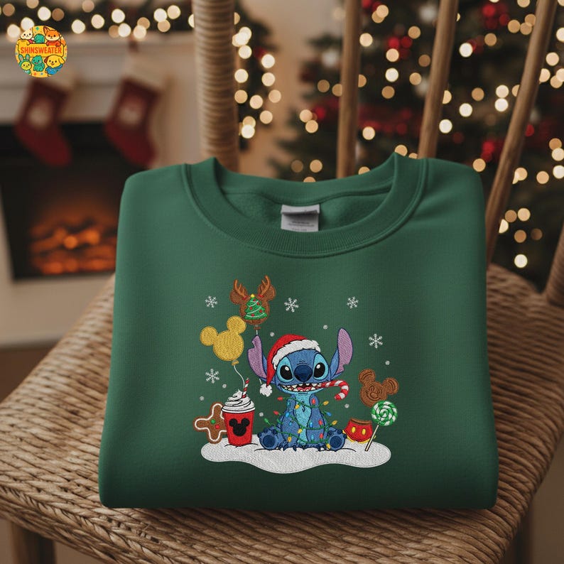 K&ouml;nnte beinhalten: Dunkelgr&uuml;nes Sweatshirt mit einem gestickten Bild von Stitch aus Lilo & Stitch, der einen Weihnachtsmannhut tr&auml;gt und von Weihnachtsdekorationen umgeben ist. Das Design umfasst Schneeflocken, Luftballons und Zuckerstangen.