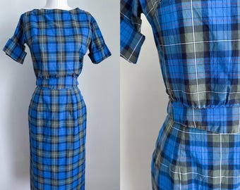 Könnte beinhalten: Ein blaues und grünes kariertes Kleid mit einem figurbetonten Rock und einem kurzärmeligen Oberteil. Das Kleid hat ein schlichtes, klassisches Design.