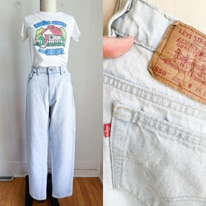 May include: A light wash denim outfit consisting of a white t-shirt and light blue jeans. The t-shirt has a graphic of a house and the words "Better Homes and Gardens". The jeans have a Levi Strauss tag.