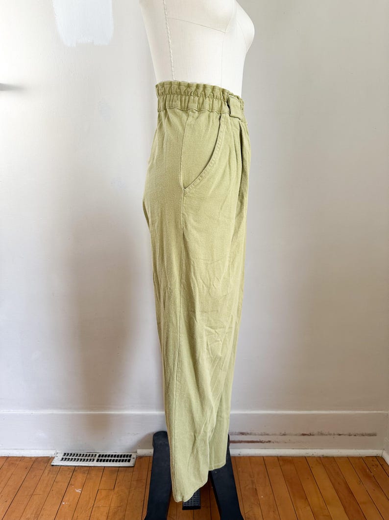 May include: Light green pants with an elastic waistband and a single pocket. The pants are made of a soft, flowing fabric and have a relaxed fit. The pants are displayed on a mannequin.