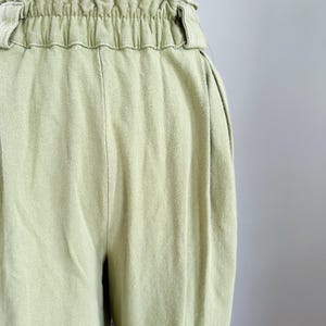 May include: Close-up of light green pants with an elastic waistband. The pants have a relaxed fit and a soft, textured appearance. The fabric appears to be a lightweight material, suitable for casual wear. The pants are displayed on a mannequin.