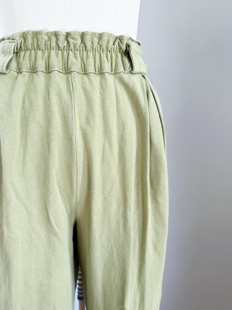 May include: Close-up of light green pants with an elastic waistband. The pants have a relaxed fit and a soft, textured appearance. The fabric appears to be a lightweight material, suitable for casual wear. The pants are displayed on a mannequin.