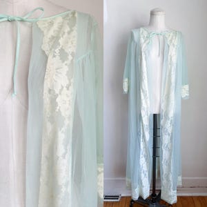 May include: A light blue vintage robe with white lace trim. The robe is sheer and has long sleeves. The lace trim is along the front opening, cuffs, and neckline. The robe is displayed on a mannequin.