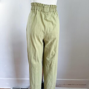 May include: Light green high-waisted pants with a gathered waistband and a belt loop. The pants are made of a textured fabric and have a straight leg design. The pants are displayed on a mannequin.