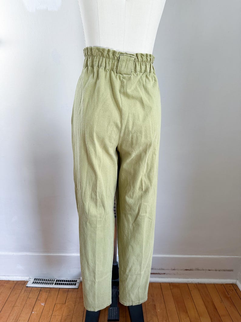 May include: Light green high-waisted pants with a gathered waistband and a belt loop. The pants are made of a textured fabric and have a straight leg design. The pants are displayed on a mannequin.
