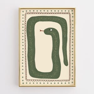 Könnte beinhalten: Gerahmter Kunstdruck mit einer stilisierten grünen Schlangenillustration. Die Schlange ist in einer Schleifenform auf cremefarbenem Hintergrund dargestellt, mit roter Zunge und kleinem Auge. Der goldene Rahmen hat einen gepunkteten Rand.