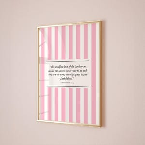 Puede incluir: Obra de arte enmarcada con un marco dorado. La impresión presenta un fondo a rayas rosas y blancas con un cuadro de texto rectangular. El texto dice: "El amor constante del Señor nunca cesa; sus misericordias nunca terminan; son nuevas cada mañana; grande es tu fidelidad."