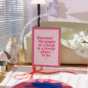 May include: A framed pink print with the text "Between the pages of a book is a lovely place to be." The print is in a room with a rug, a sofa, and a lamp.