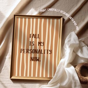 Peut inclure: Une affiche encadr&eacute;e aux couleurs chaudes. L'&oelig;uvre pr&eacute;sente des rayures verticales beiges et marron. Le texte "FALL IS MY PERSONALITY NOW" est affich&eacute; en marron fonc&eacute;. Le cadre est dor&eacute;.