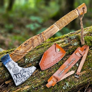 May include: A survival axe with a scorched wooden handle wrapped in twine and a metal head featuring etched Norse-style runes and skull imagery. Includes a tan leather sheath and a leather belt strap embossed with the text Handmade Forged Survival Axe.