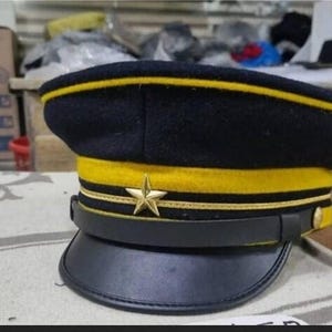 May include: A black and yellow military style hat with a gold star on the front. The hat has a black leather band and a yellow brim.