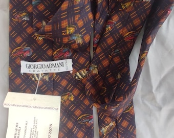 May include: A dark purple silk tie with a repeating pattern of colorful abstract shapes and a grid design. The tie has a Giorgio Armani label and a tag with text.