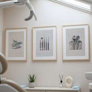 Framed vintage illustration of three teeth hanging above white chairs in a dentist waiting area, minimalistic wall art decor.