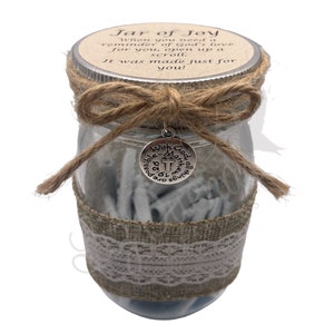 May include: A glass jar with a brown burlap ribbon and a silver charm that says "With God all things are possible" with a cross. The jar is filled with white paper scrolls and has a brown paper lid with the text "Jar of Joy" and "When you need a reminder of God's love for you, open up a scroll. It was made just for you!"