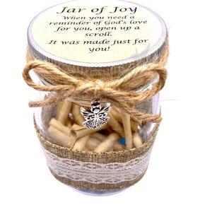 May include: A glass jar with a burlap lid and a silver angel charm. The jar is filled with small scrolls of paper and has a label that reads "Jar of Joy" and includes the text "When you need a reminder of God's love for you, open up a scroll. It was made just for you!"