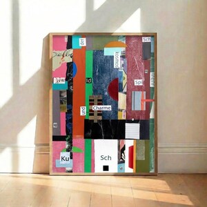 May include: Abstract art print in a wooden frame. The artwork is a collage of colorful paper strips and shapes, including pink, green, blue, and red. Some text fragments are visible. The artwork is displayed on a wooden floor against a white wall.