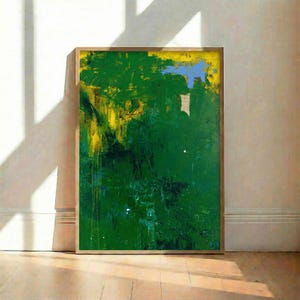 Puede incluir: Pintura abstracta enmarcada en madera. La obra presenta una vibrante mezcla de pinceladas verdes, amarillas y azules. La pintura tiene una apariencia texturizada, con capas de pintura visibles. La obra se exhibe contra una pared blanca y un suelo de madera.