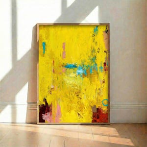 Puede incluir: Obra de arte abstracta con un fondo amarillo vibrante, acentuado por trazos de azul, rosa y rojo. La obra está enmarcada en un marco de madera natural, creando un contraste llamativo. Se exhibe contra una pared blanca.