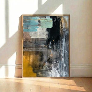 May include: Abstract art print in a wooden frame. The artwork features a mix of colors, including yellow, black, gray, and blue. A section of text is visible in the upper center. The painting has a textured appearance, with visible brushstrokes.