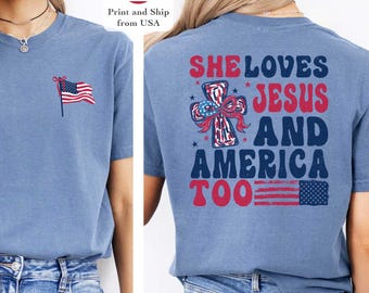 May include: Blue short-sleeved t-shirt with a small American flag graphic on the front and the text "SHE LOVES JESUS AND AMERICA TOO" on the back. The shirt is a light blue color and is paired with blue jeans.