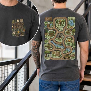 May include: Dark gray t-shirt with a graphic on the front that says "Tired Dads Club". The back of the shirt features a colorful map design labeled "Backyard Expedition" with various outdoor activity locations.