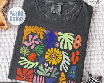 以下が含まれることがあります： カラフルな花柄が特徴のダークグレーのComfort Colors Tシャツ。オレンジ、ピンク、イエロー、ブルー、グリーンの抽象的な花と葉のデザイン。クルーネックと半袖。下部に「Pepper」の文字。