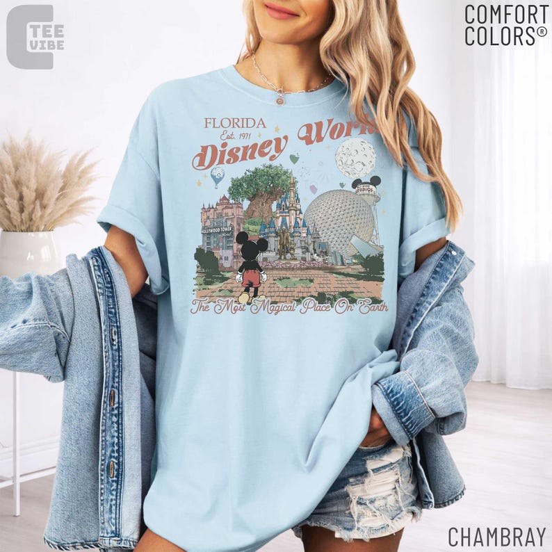 May include: Light blue t-shirt with a graphic of Disney World in Florida. The design includes Mickey Mouse, a castle, and the text "Disney World" and "The Most Magical Place On Earth". The shirt is a Comfort Colors brand.