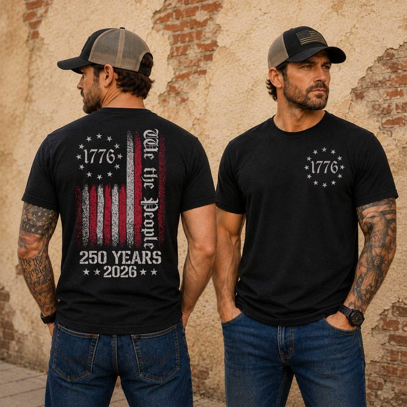 May include: Two black t-shirts with the American flag design. One shirt features the flag on the back with "1776", "We the People", and "250 Years 2026". The other shirt has "1776" in a circle of stars on the front. Both shirts are worn with a baseball cap.