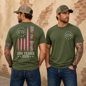 May include: Olive green t-shirts with a distressed American flag design and the text "1776" and "We the People". The back of the shirt also features "250 YEARS 2026". The models are wearing baseball caps.