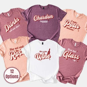 May include: A collection of six t-shirts in various colors, each with a wine-themed graphic. The shirts feature phrases like "Drinks well with others," "Chardon," and "Like a fine Wine." The image also includes a button that says "12 Options."
