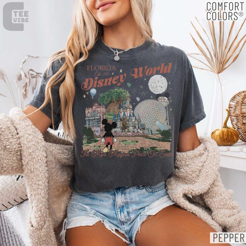 May include: Dark gray t-shirt with a Disney World graphic. The design features Mickey Mouse, the Tree of Life, Cinderella's Castle, and Spaceship Earth. Text includes "Florida Est. 1971 Disney World" and "The Most Magical Place On Earth."