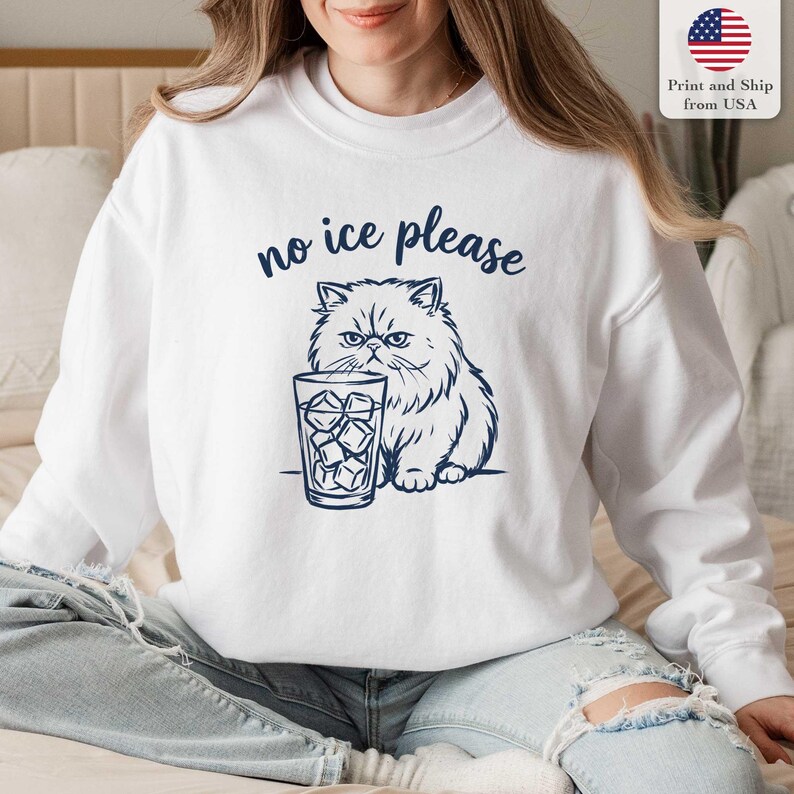 Puede incluir: Sudadera blanca con un gr&aacute;fico azul marino de un gato persa y un vaso de hielo. El texto "no ice please" est&aacute; encima del gato. La sudadera tiene cuello redondo y mangas largas. El gr&aacute;fico est&aacute; impreso en la parte delantera.