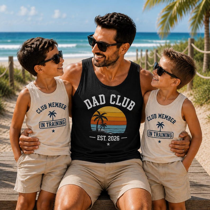 以下が含まれることがあります： 夕日のグラフィックと「DAD CLUB EST. 2026」の文字が入った黒のタンクトップと、「CLUB MEMBER IN TRAINING」の文字とヤシの木のグラフィックが入ったベージュのタンクトップ2枚。3着ともラウンドネックで袖なしのデザインです。