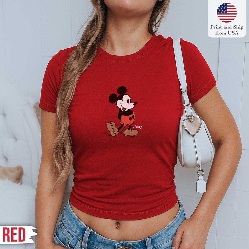 May include: A red t-shirt featuring a classic Mickey Mouse graphic. The cartoon character is depicted in his iconic pose, with black ears, a white face, red shorts, and brown shoes. The shirt also has the text "Disney" below the character. The text "Print and Ship from USA" is also visible.